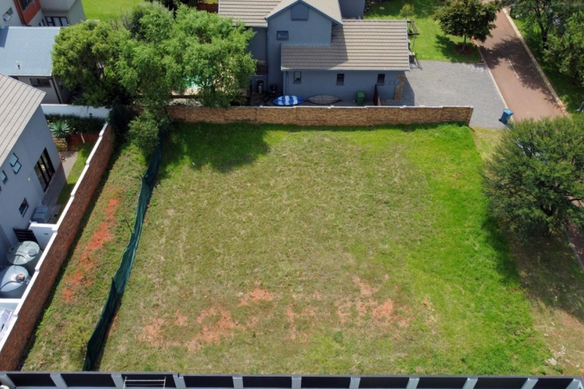 An aerial view of a vacant residential plot featuring a grass lawn, enclosed by boundary walls and fencing in a developed neighborhood.