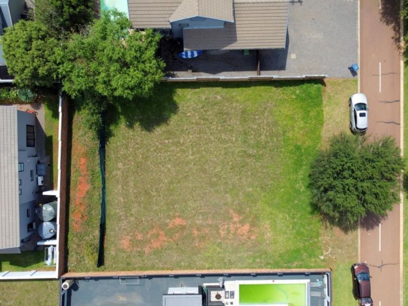 An aerial view of a vacant residential plot situated between existing properties, featuring established trees and boundary fencing.