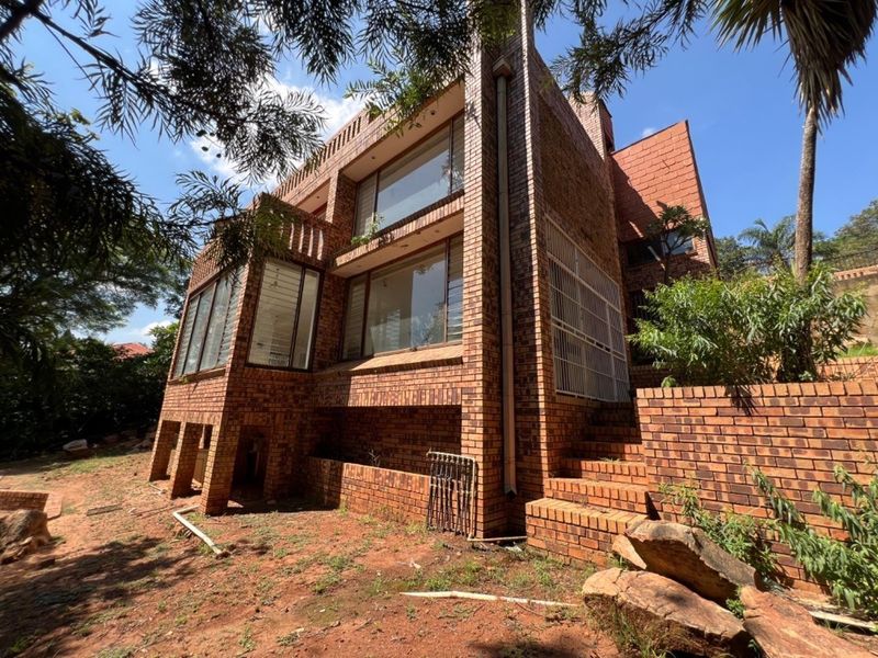 Rear view of a multi-story face brick house featuring large windows, a brick staircase, and an expansive, unlandscaped garden area.
