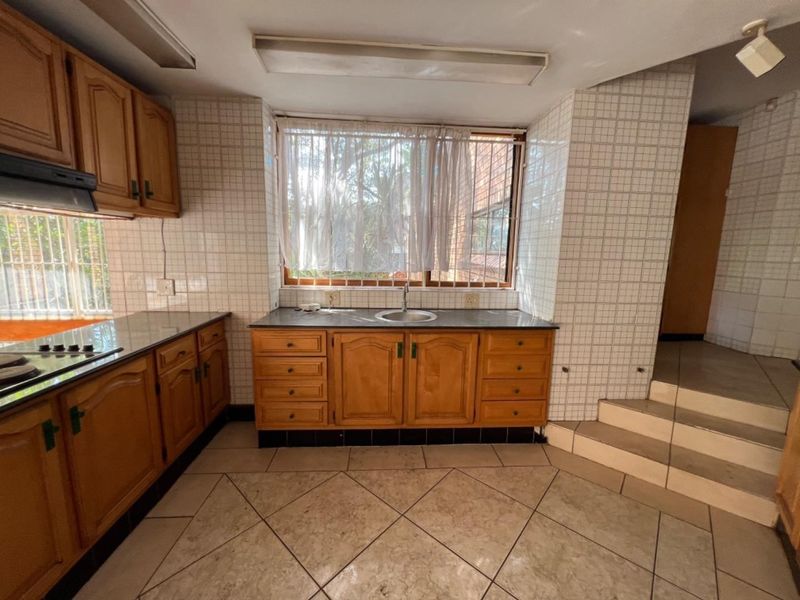 A functional kitchen featuring wooden cabinetry, granite countertops, built-in hob, and tiled finishes, offering a classic layout with potential for modern updates.