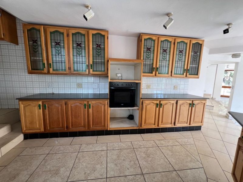 A spacious kitchen featuring traditional wooden cabinetry with leaded glass accents, built-in oven, stone countertops, and neutral tiled flooring.