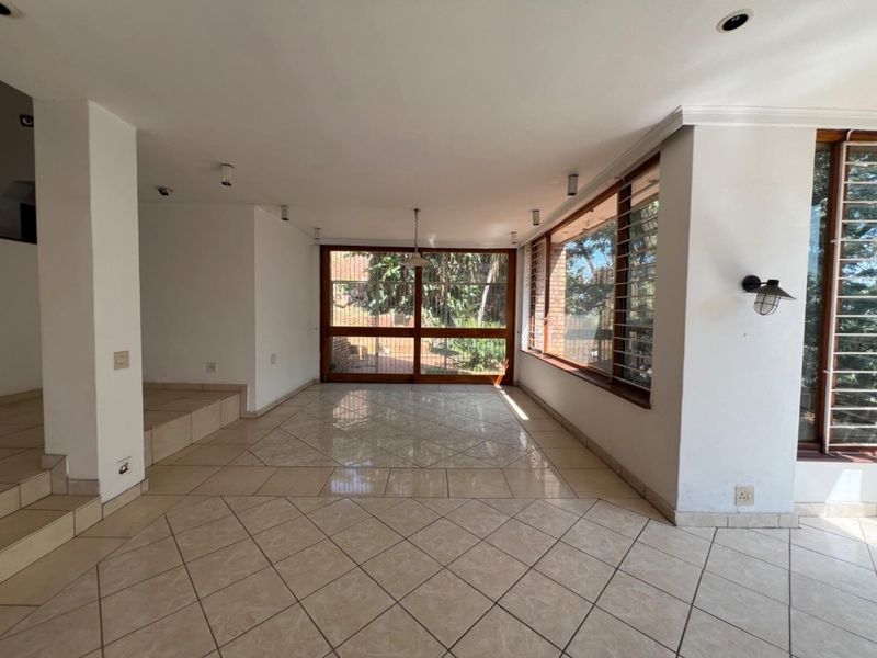 Spacious, light-filled living area featuring neutral tiled flooring, recessed lighting, and large timber-framed windows with security bars, offering a seamless transition to the outdoors.