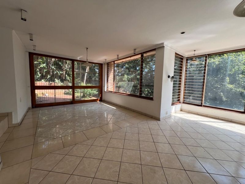 Spacious, sunlit living area featuring large windows with garden views, tiled flooring, and direct access to the outdoor space.