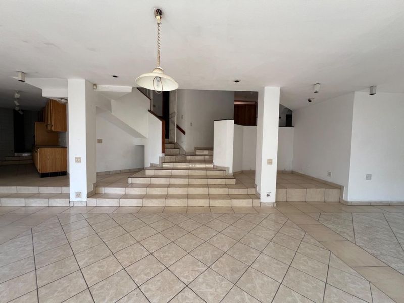Spacious open-plan living area featuring tiled flooring, a central staircase, and integrated kitchen cabinetry, offering a versatile layout for renovation.