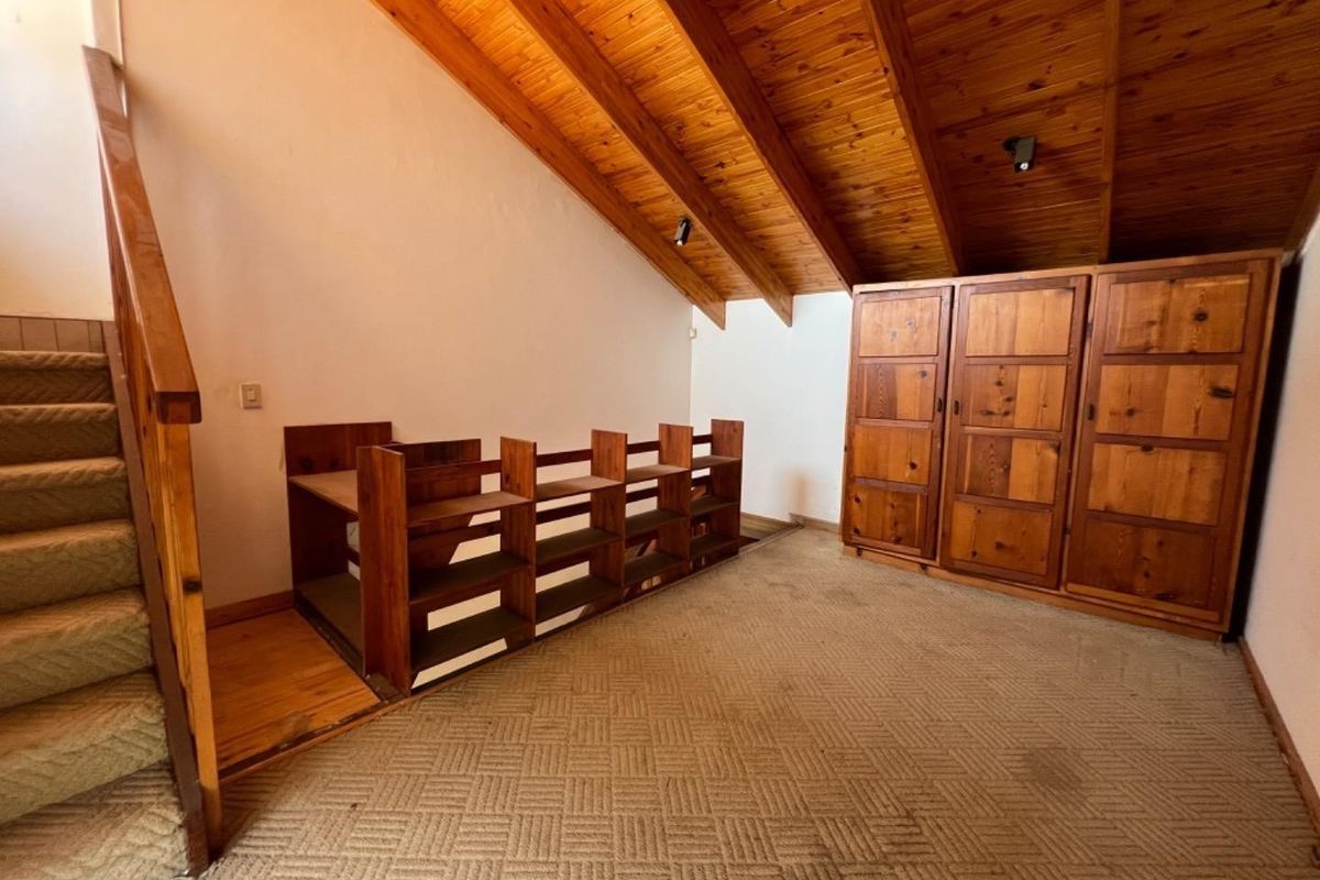 Bedroom featuring a vaulted timber ceiling, built-in wooden wardrobe, and carpeted flooring, offering a rustic aesthetic with potential for modernization.