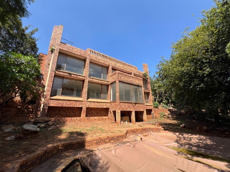 Rear view of a multi-story face brick house featuring large windows, a swimming pool, and established garden surroundings.