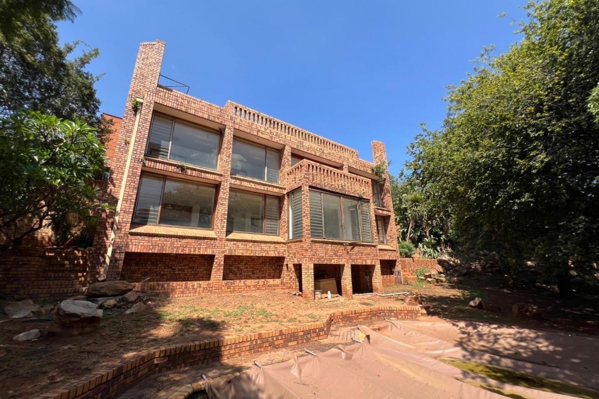 Rear view of a multi-story face brick house featuring large windows, a swimming pool, and established garden surroundings.
