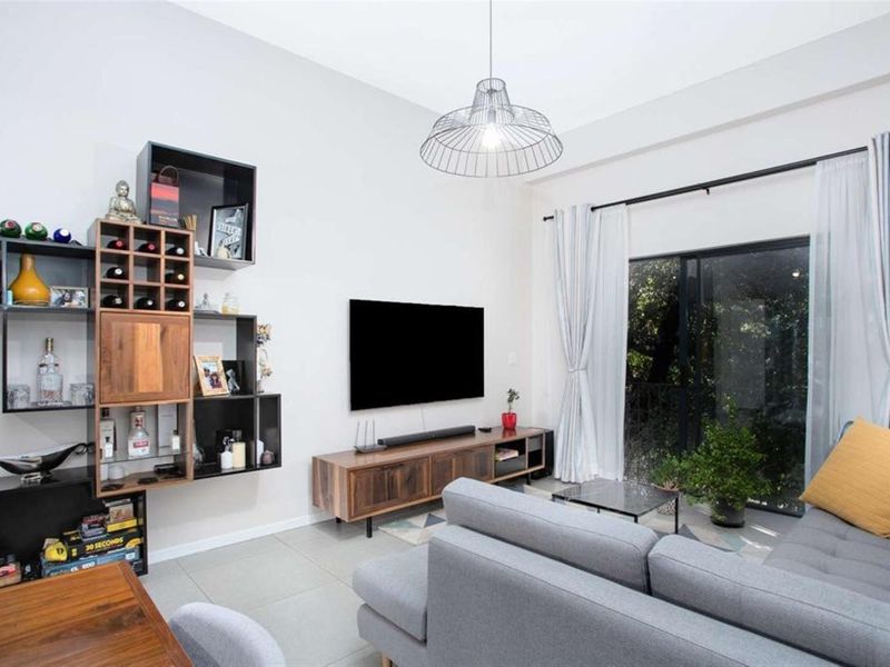 A bright and modern living room featuring tiled flooring, a large sliding glass door providing natural light, and a contemporary pendant light fixture.