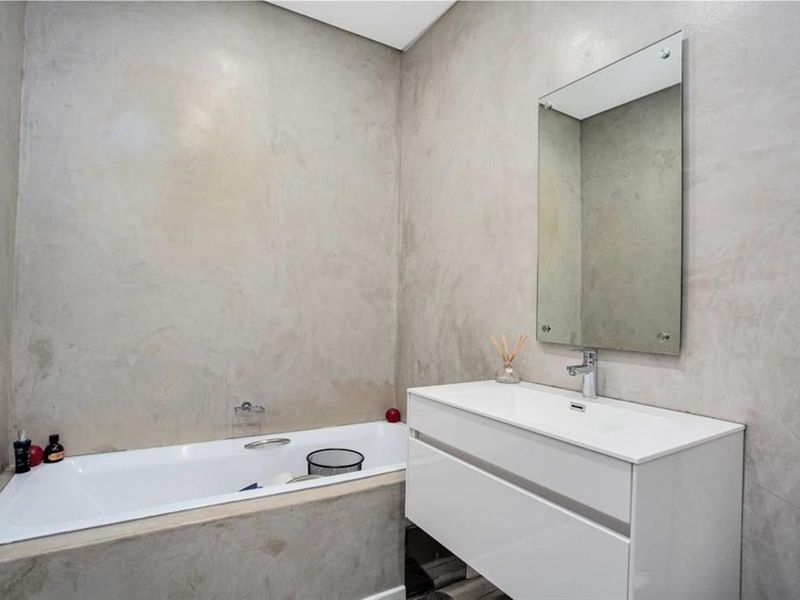 Modern bathroom featuring a built-in bathtub, wall-mounted vanity with integrated basin, and contemporary cement-finish walls.