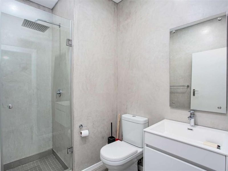 Modern bathroom featuring a glass-enclosed shower with a rain shower head, a sleek vanity with a basin, and a wall-mounted mirror.
