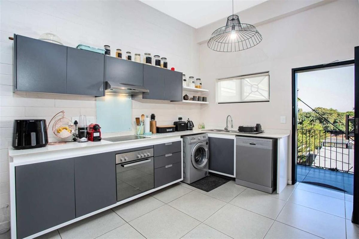 Modern kitchen featuring dark grey cabinetry, built-in oven and hob, integrated laundry and dishwasher connections, and direct access to a balcony.
