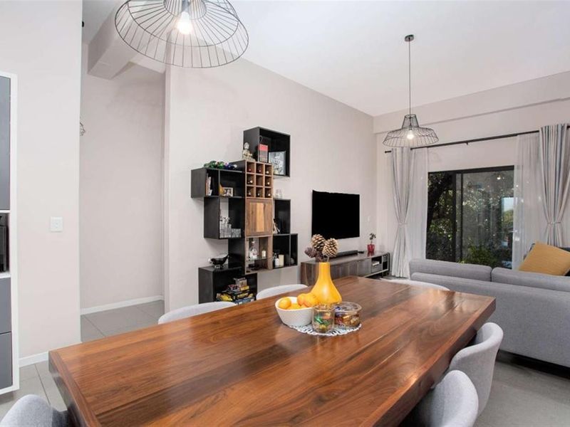 A bright open-plan living and dining area featuring tiled floors, modern pendant lighting, and large sliding glass doors leading to an outdoor space.