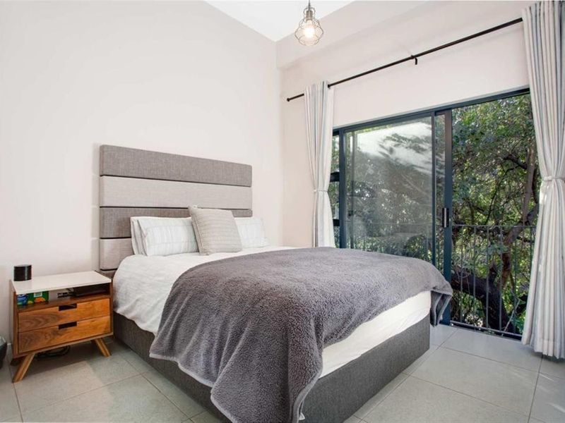 A well-lit bedroom featuring tiled flooring and a large sliding glass door that opens to a balcony with lush green views.