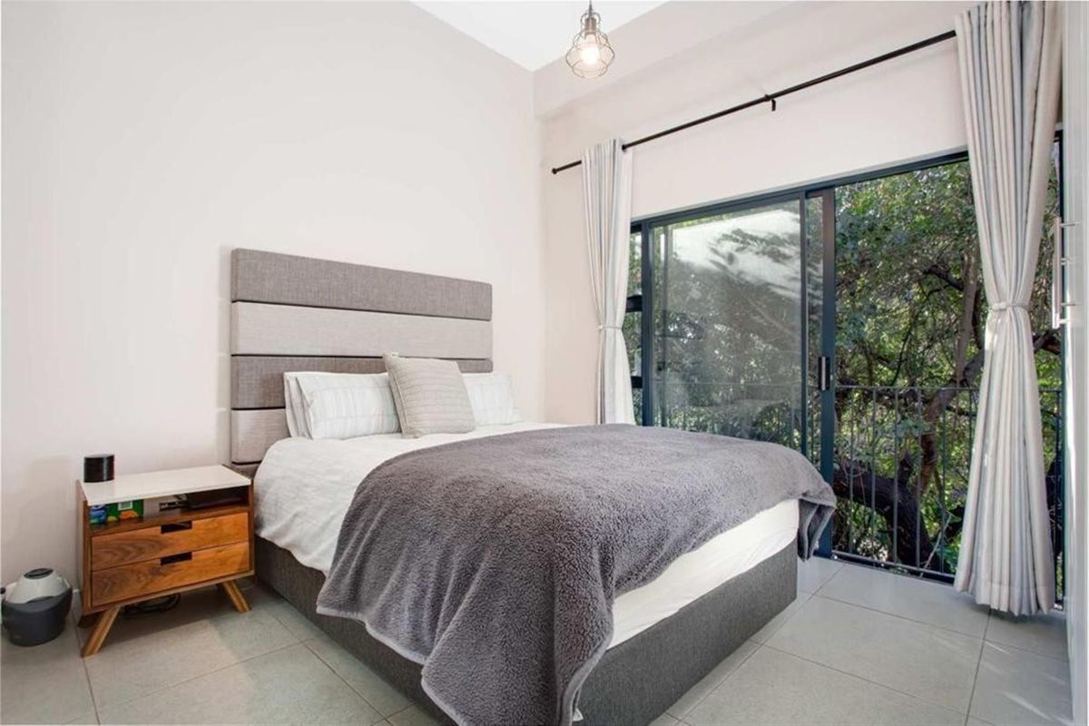 A well-lit bedroom featuring tiled flooring and a large sliding glass door that opens to a balcony with lush green views.