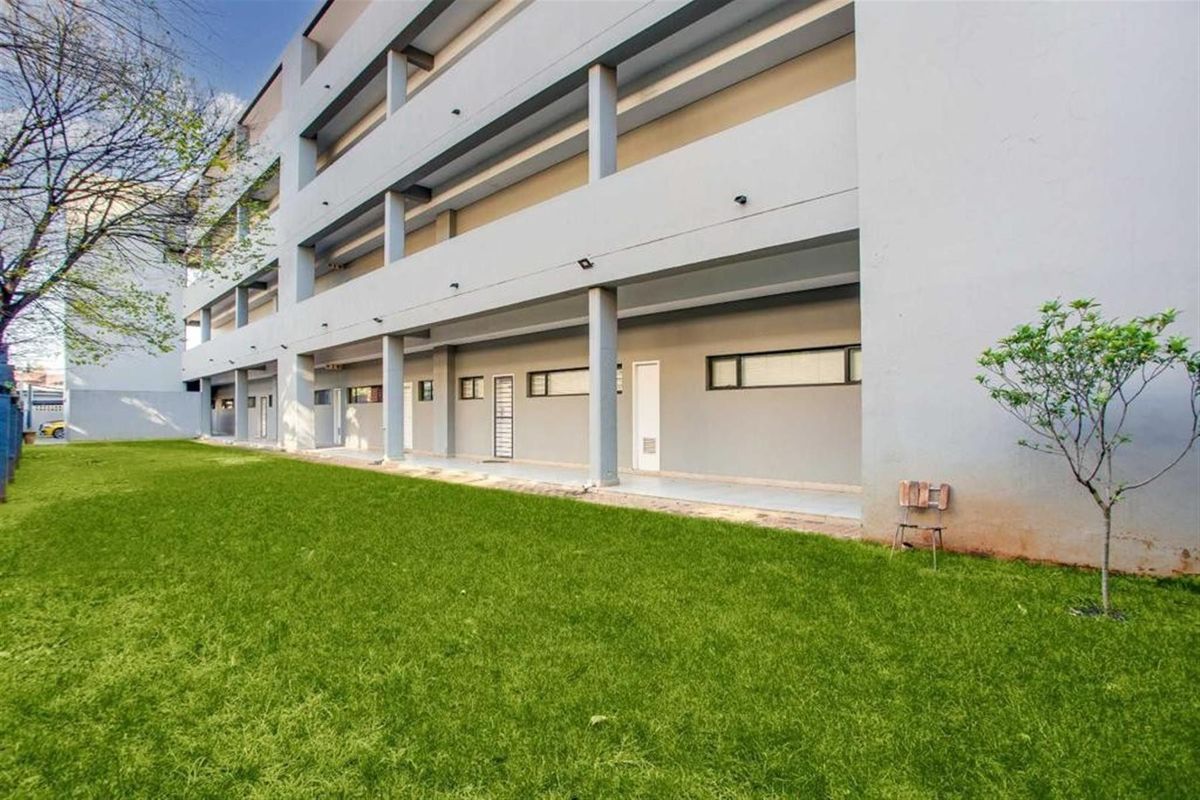 A view of the apartment building exterior featuring a covered walkway, concrete pillars, and a well-maintained lawn area.