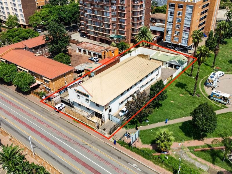 Aerial view of a commercial property featuring a metal-roofed building, perimeter fencing, and paved driveway access situated in an urban environment.