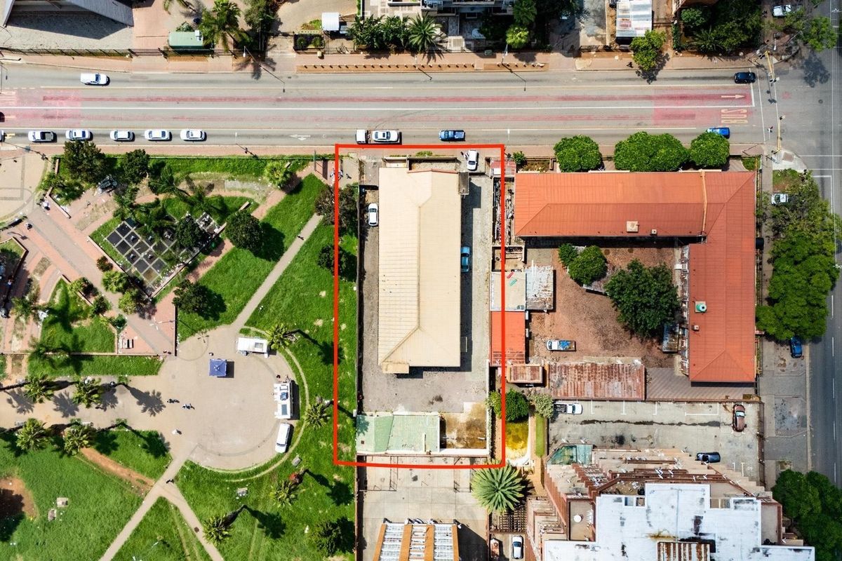 Aerial view of a commercial property featuring a main building with a metal roof, paved yard area, and perimeter boundary walls.