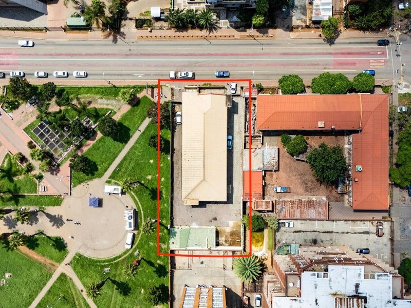 Aerial view of a commercial property featuring a main building with a metal roof, paved yard area, and perimeter boundary walls.