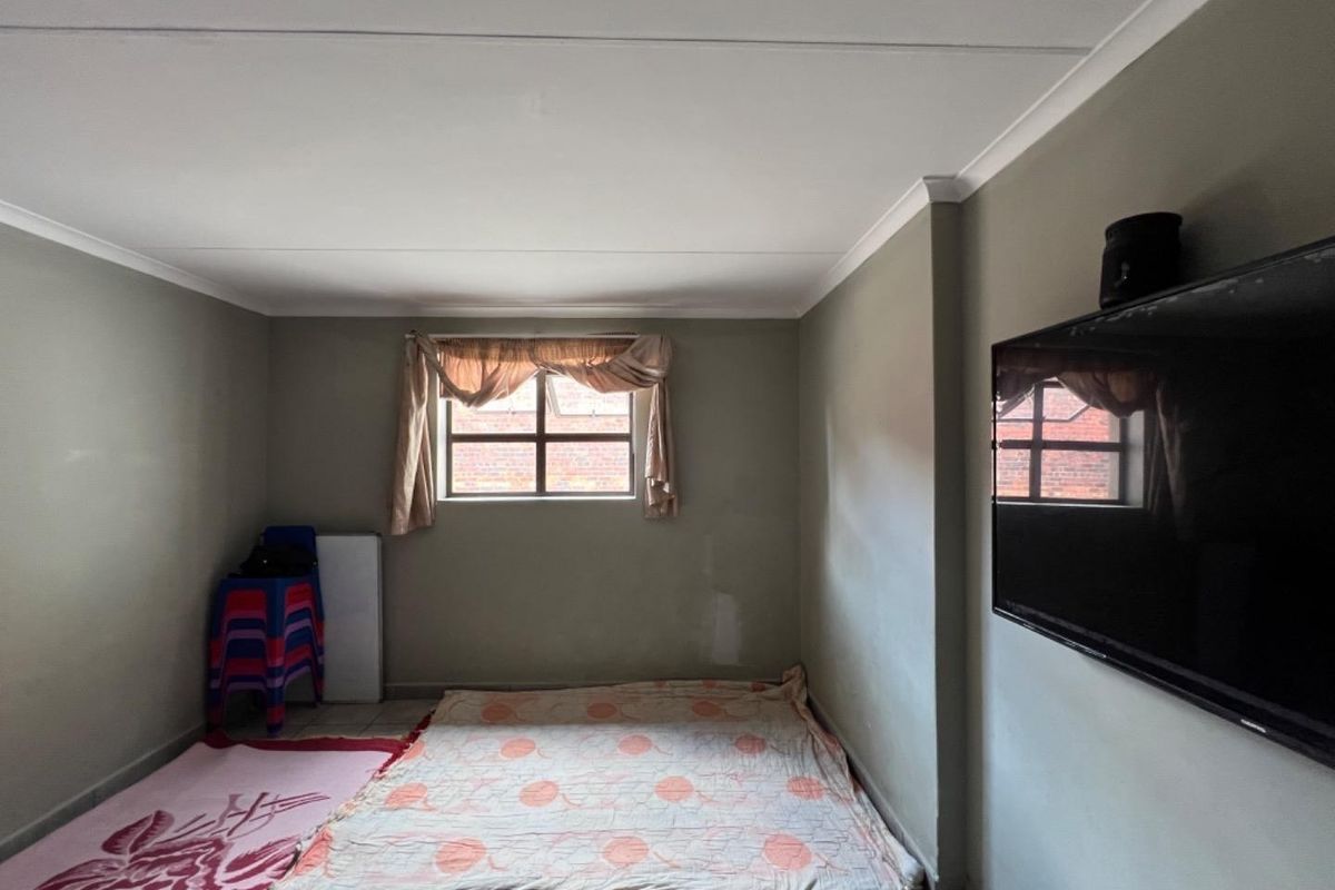 A simple living area featuring tiled flooring, coved ceilings, and a window, currently presented as an empty space with neutral wall finishes.
