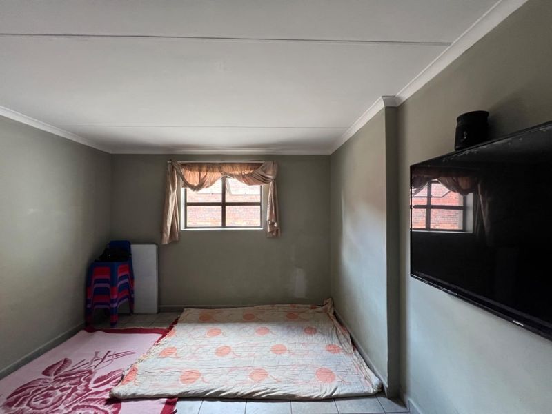 A simple living area featuring tiled flooring, coved ceilings, and a window, currently presented as an empty space with neutral wall finishes.