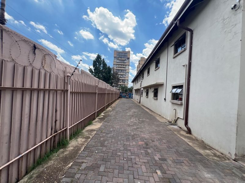 A paved side access path between a commercial building and a secure perimeter fence with razor wire.