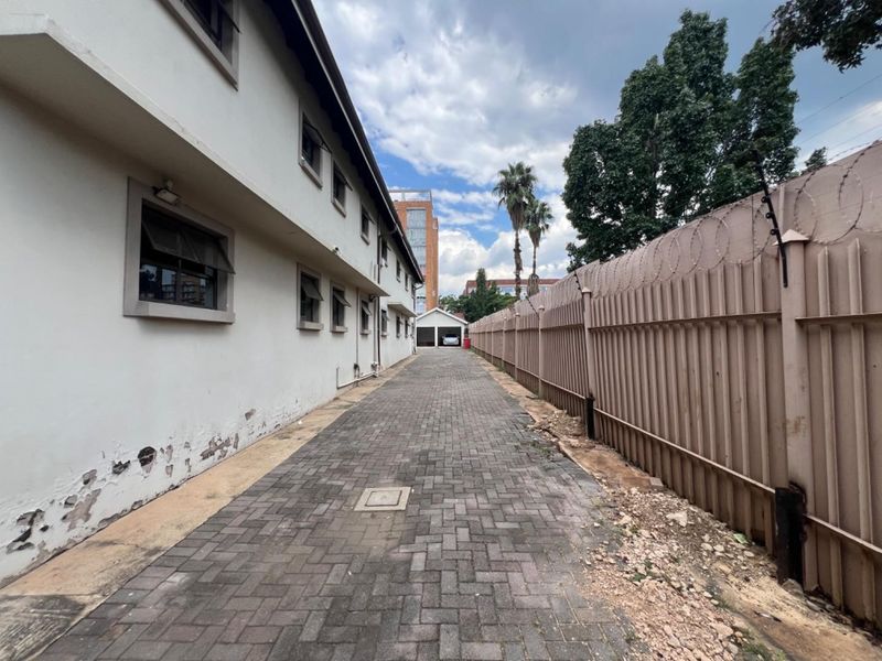 A paved side driveway leading to a rear garage, featuring perimeter fencing with razor wire and exterior wall maintenance required.