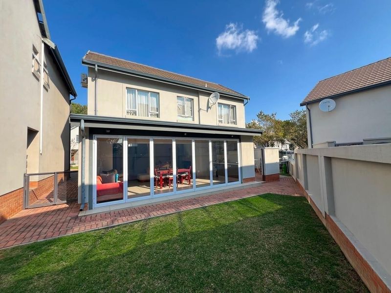 Rear view of a two-story house featuring a paved patio, small lawn, and large bi-fold doors leading into the living area.