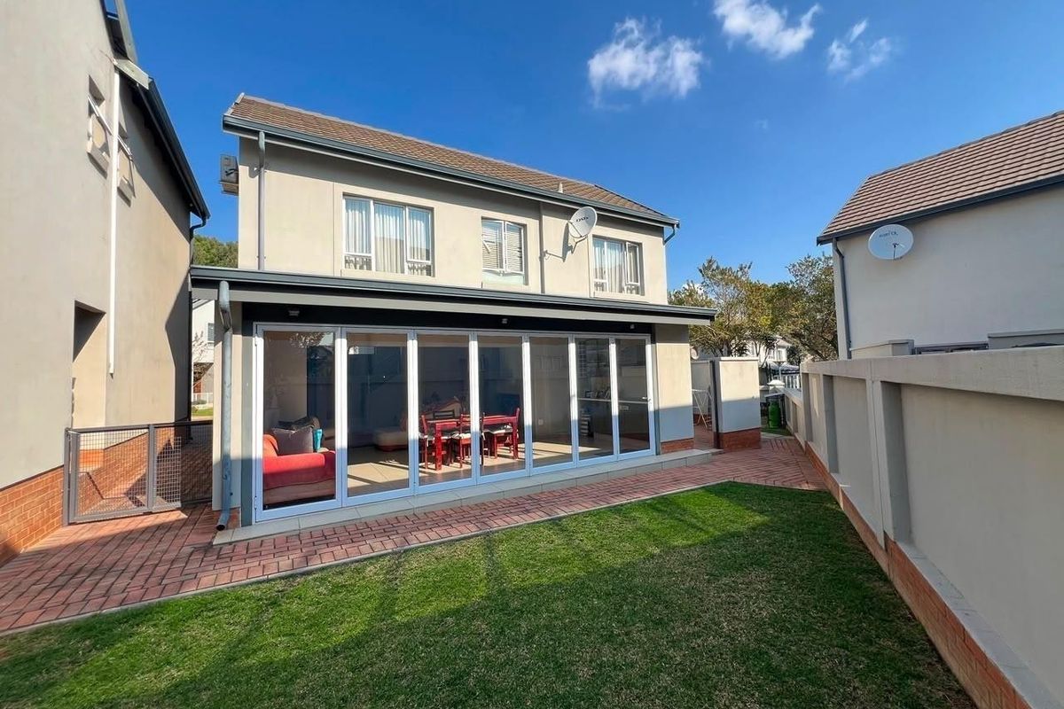 Rear view of a two-story house featuring a paved patio, small lawn, and large bi-fold doors leading into the living area.