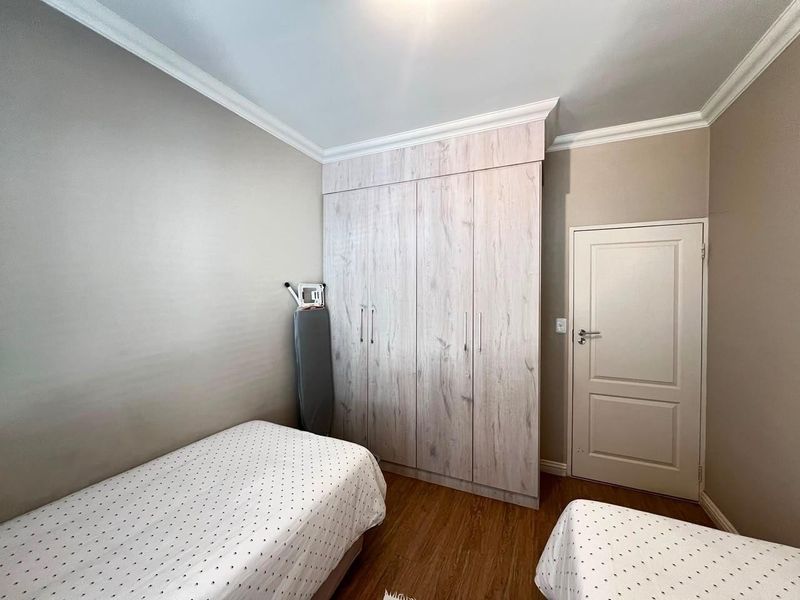 A well-maintained bedroom featuring light wood-grain built-in wardrobes, laminate flooring, and classic crown molding details.
