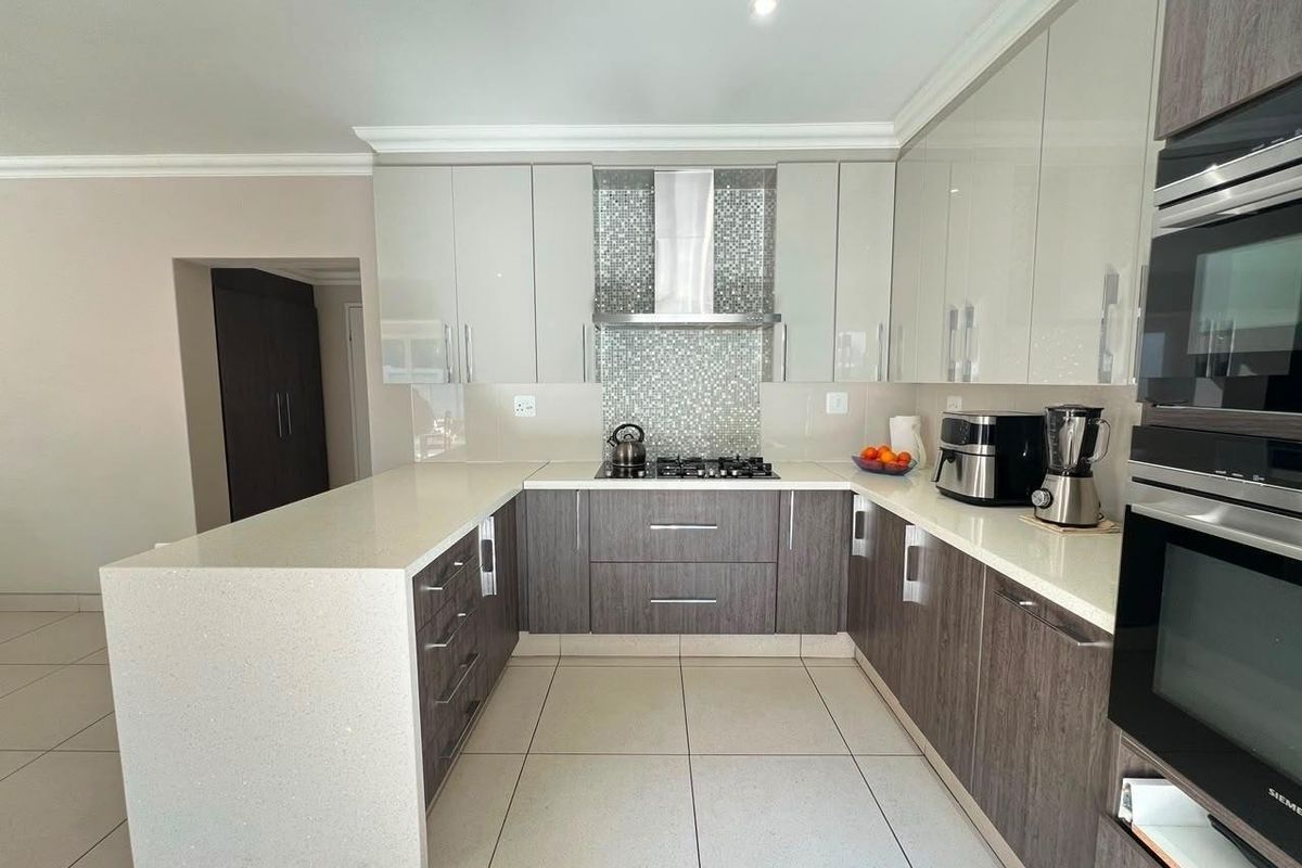 Modern kitchen featuring high-gloss cabinetry, quartz countertops, a gas hob with stainless steel extractor, and integrated Siemens appliances.