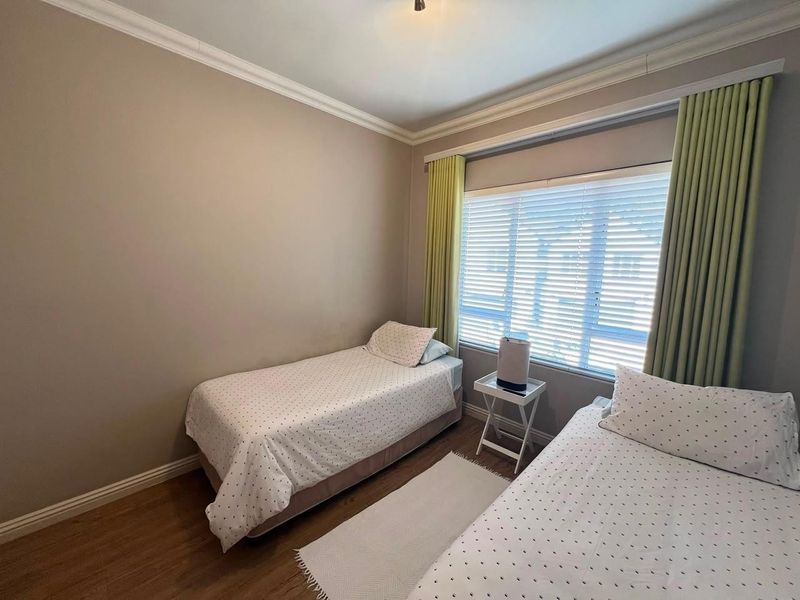A well-maintained bedroom featuring laminate flooring, crown molding, and large windows with fitted venetian blinds.