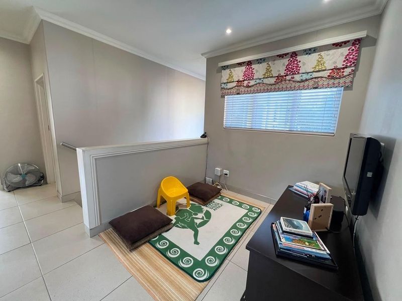 A landing or hallway area featuring tiled flooring, a staircase balustrade, and recessed lighting, currently utilized as a casual seating space.