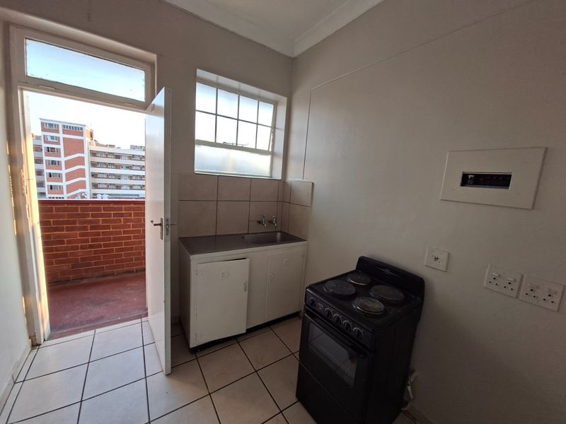 A compact kitchen area featuring tiled flooring, a stainless steel sink with tiled splashback, and direct access to an outdoor balcony.