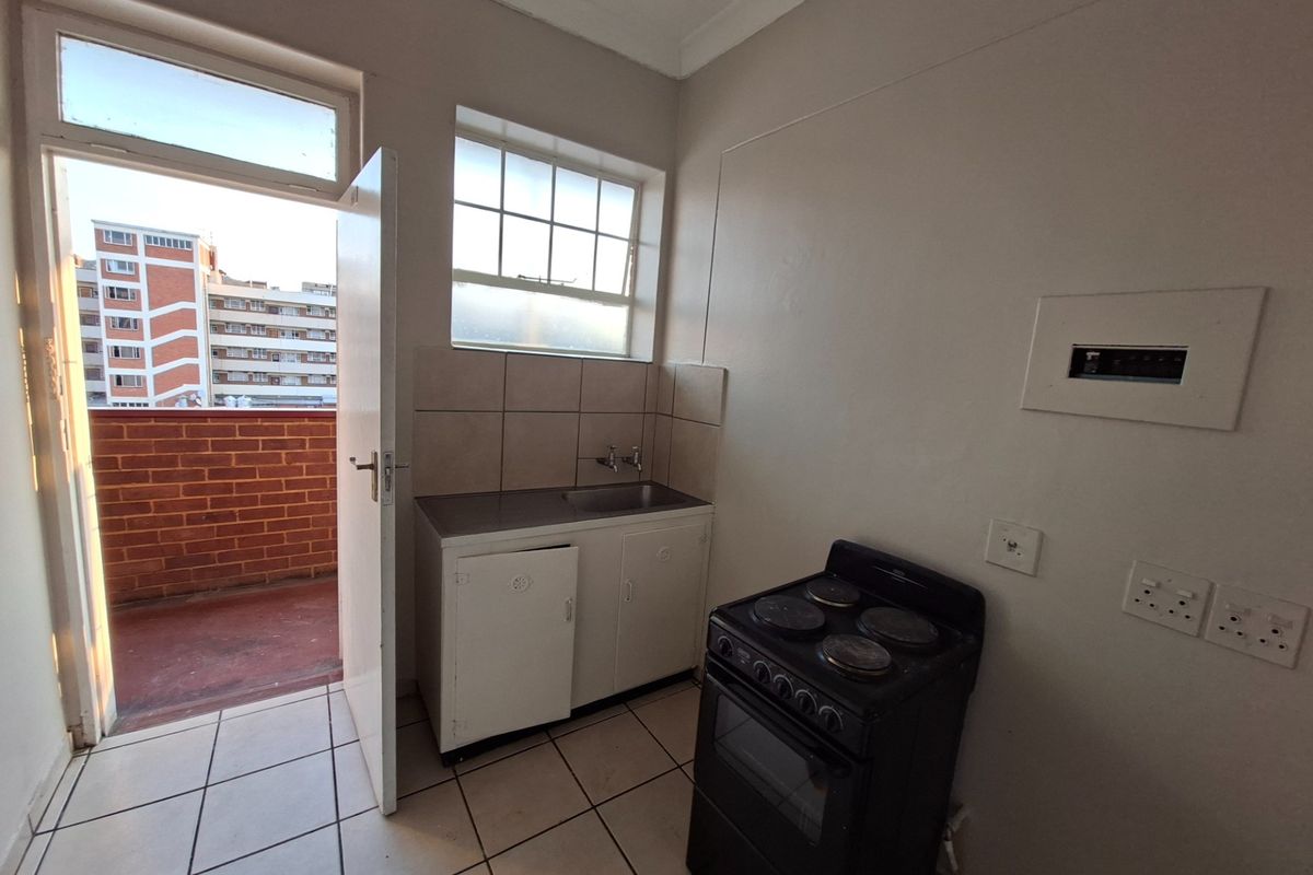A compact kitchen area featuring tiled flooring, a stainless steel sink with tiled splashback, and direct access to an outdoor balcony.