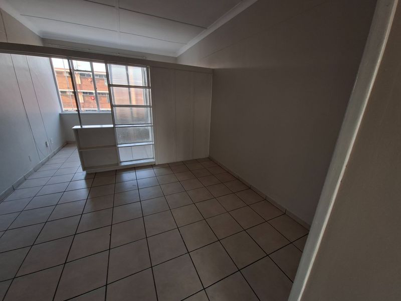 An empty bedroom featuring tiled flooring, a built-in wardrobe, and a partition wall, offering a clean and versatile space.