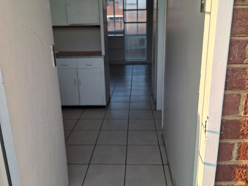 A view through a doorway into a tiled hallway leading to a kitchen area with built-in cabinetry and a glass sliding door.