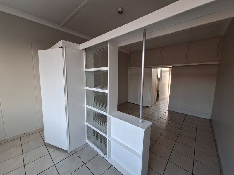 An empty bedroom featuring tiled flooring, built-in cupboards, overhead storage, and a decorative fluted glass room divider.