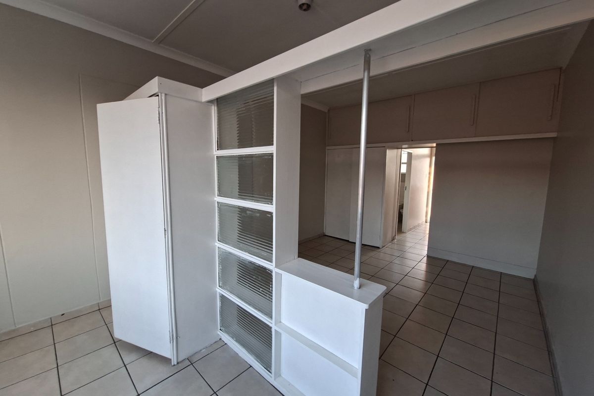 An empty bedroom featuring tiled flooring, built-in cupboards, overhead storage, and a decorative fluted glass room divider.
