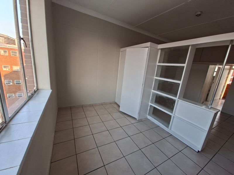 An empty bedroom featuring tiled flooring, built-in cupboards, and a unique partition wall with integrated shelving, offering a bright and functional living space.