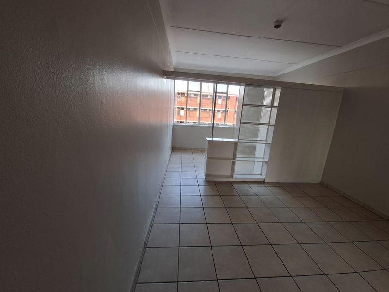 An empty, tiled living area featuring a built-in room divider and large windows, offering a blank canvas for interior design.