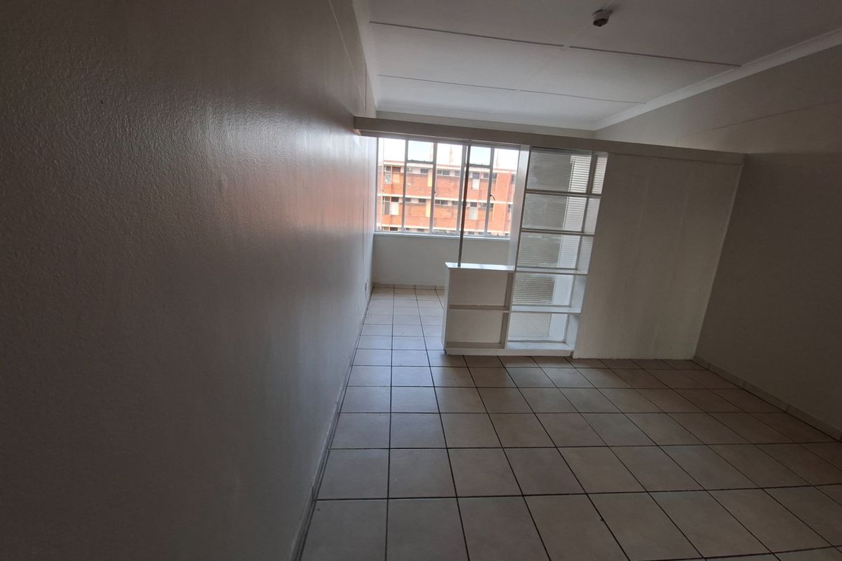 An empty, tiled living area featuring a built-in room divider and large windows, offering a blank canvas for interior design.