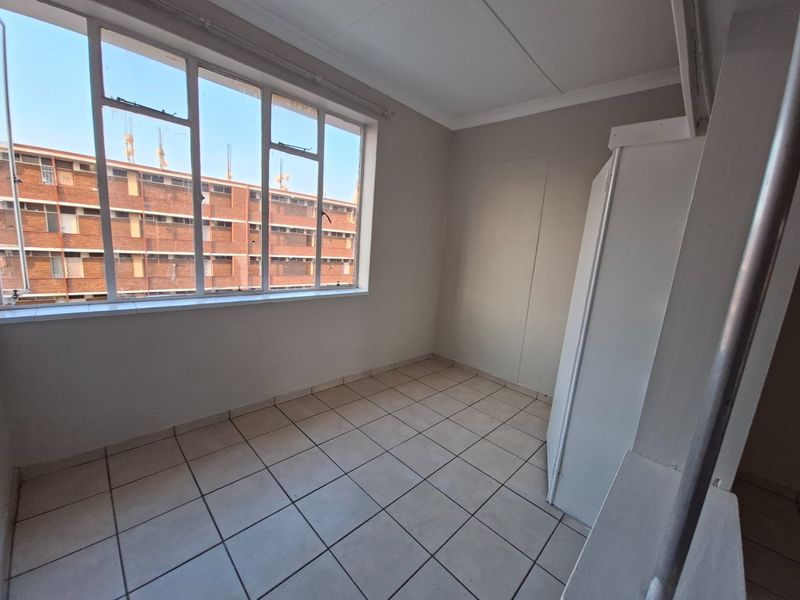 A bright, empty bedroom featuring tiled flooring, a built-in cupboard, and a large window providing natural light.