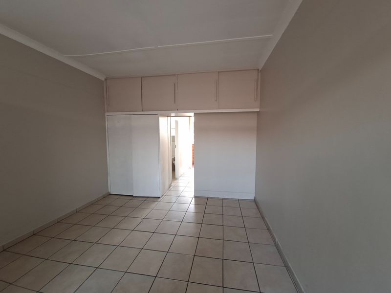 An empty bedroom featuring tiled flooring, built-in cupboards, and additional overhead storage cabinets.