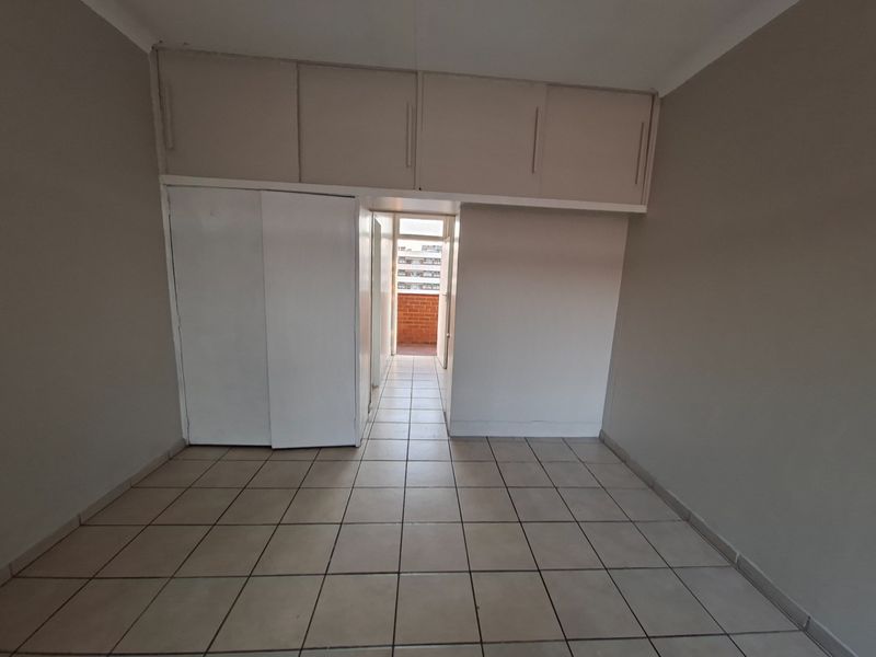 An empty bedroom featuring tiled flooring and extensive built-in cupboard storage with overhead cabinets, leading to a small balcony area.