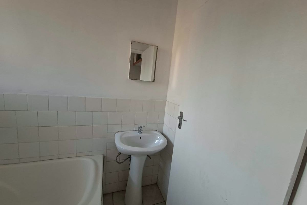 A functional bathroom featuring a pedestal washbasin, bathtub, and tiled splashback, offering a blank canvas for potential renovation and modernization.