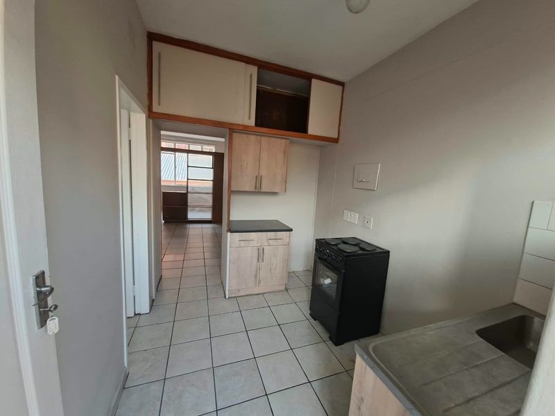 A functional kitchen area featuring tiled flooring, built-in cabinetry with overhead storage, and a freestanding stove, offering potential for modernization.