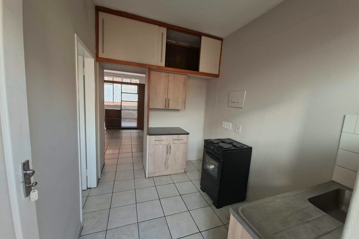 A functional kitchen area featuring tiled flooring, built-in cabinetry with overhead storage, and a freestanding stove, offering potential for modernization.