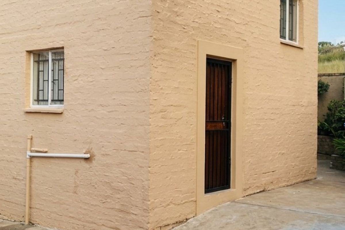 Rear exterior view of the property featuring painted brick walls, security gates, and concrete paving.