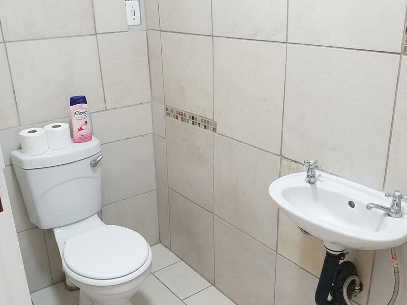 A compact guest bathroom featuring neutral wall and floor tiling, a standard toilet, and a wall-mounted basin with exposed plumbing.
