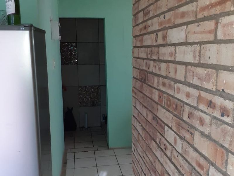 A narrow hallway featuring exposed brickwork and tiled flooring, leading into a secondary utility or bathroom area.
